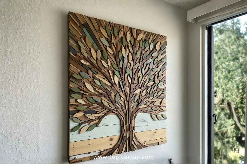 A stunning DIY wood mosaic art piece in the shape of a tree, with leaves and trunk made from small, repurposed wood scraps in brown, green, and blue tones.